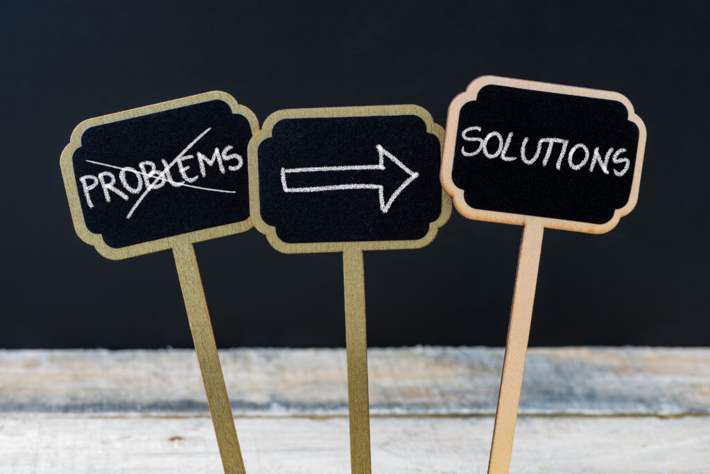 Concept message SOLUTIONS NOT PROBLEMS written with chalk on wooden mini blackboard labels, defocused chalkboard and wood table in background