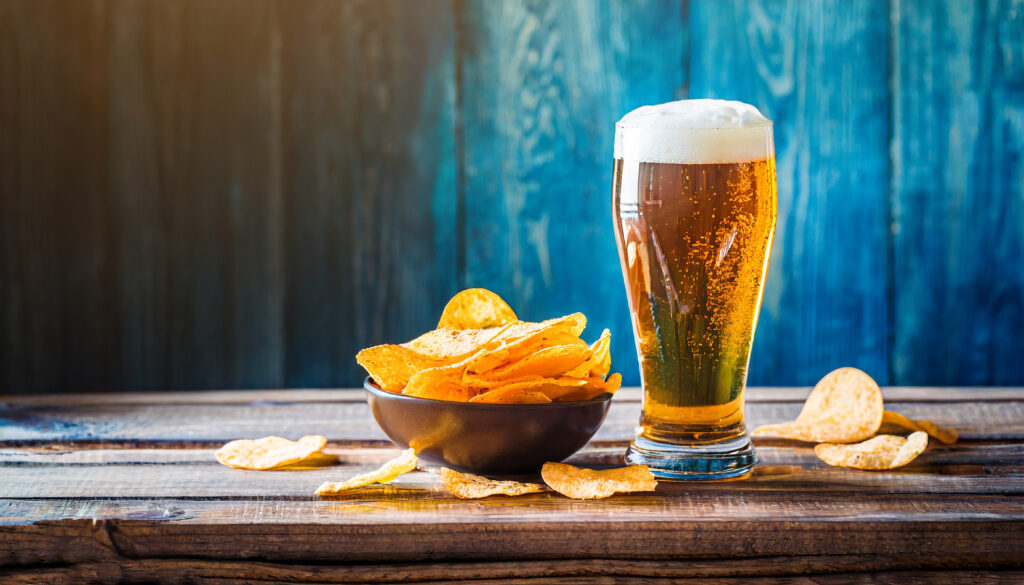 Light foamy beer with potato crisps on wooden table background, chips snack and cold bar beverage, food and drink