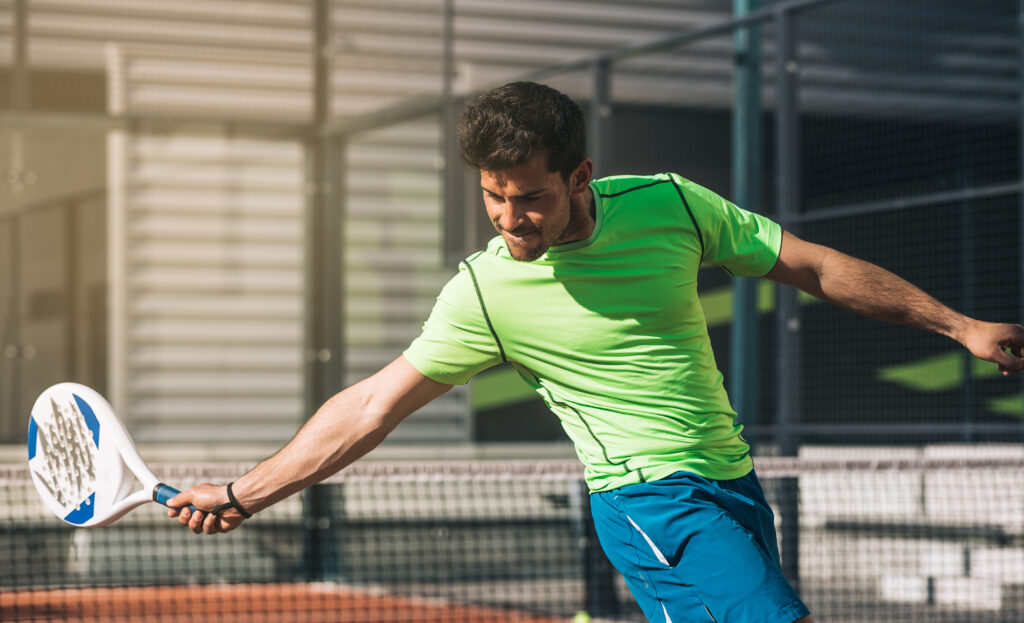 Man playing padel in a orange grass padel court outdoors behind the net